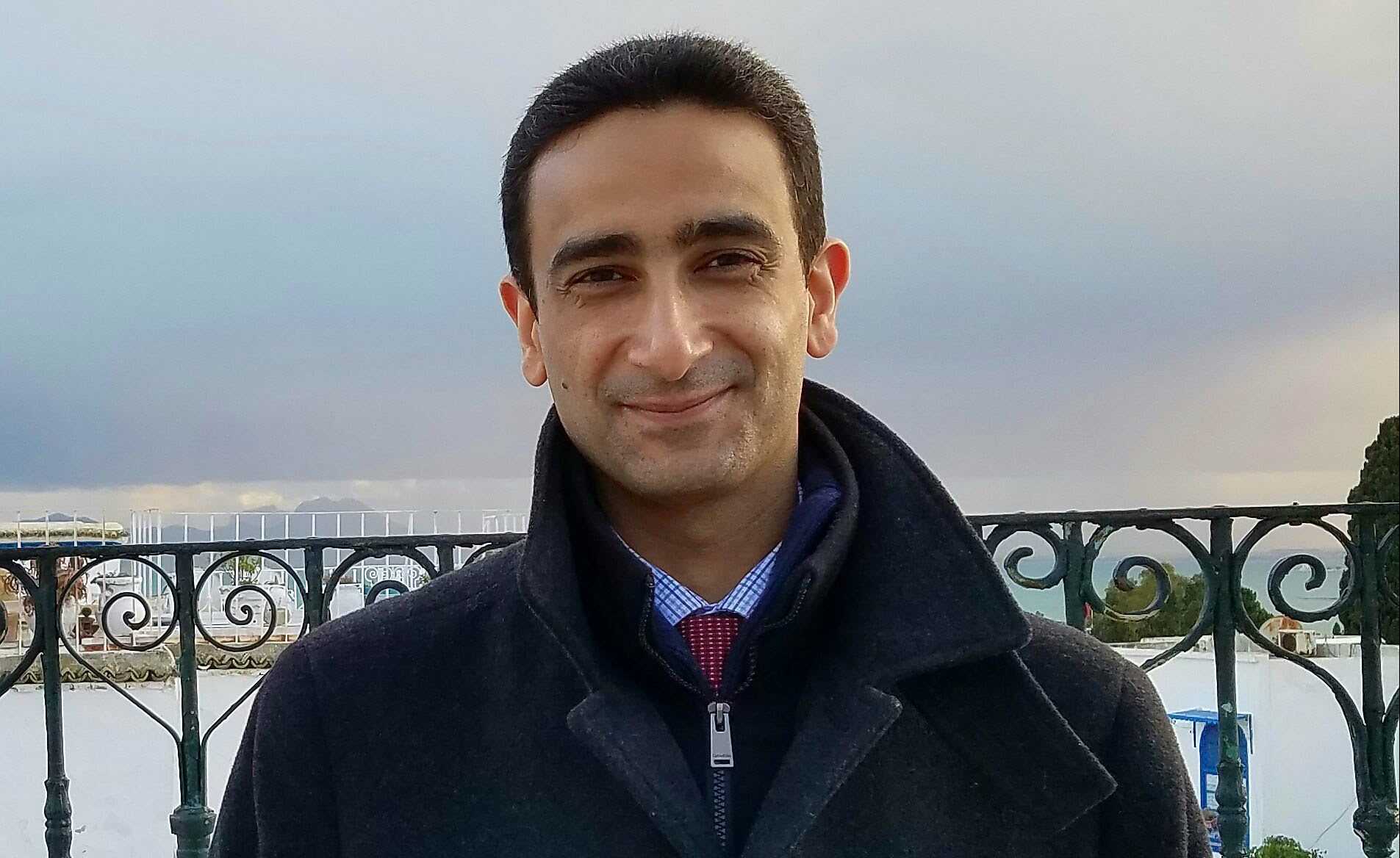 Tofigh Maboudi smiling in front of a wrought iron fence outside
